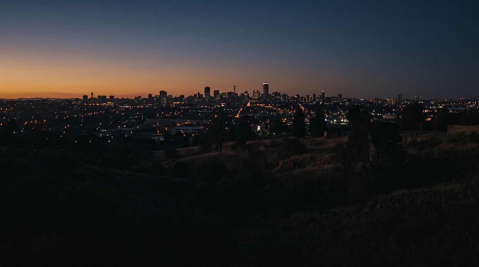 The Johannesburg skyline at blue hour, with city lights and an amber glow on the horizon.